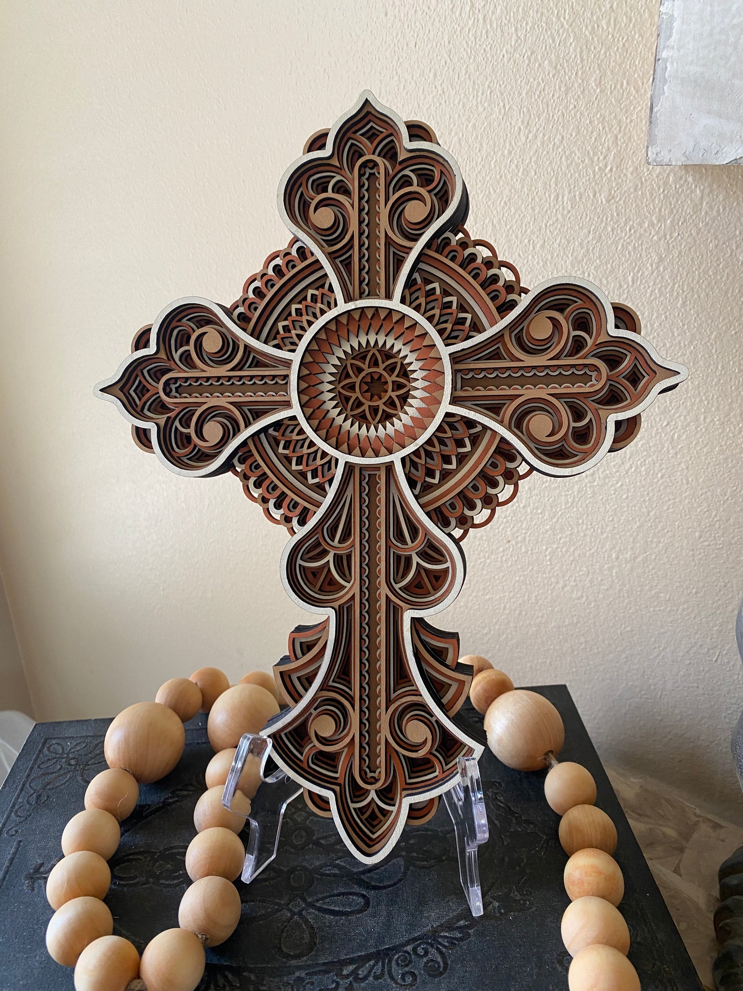 Decorative wooden cross with intricate laser cut design on a neutral wall.